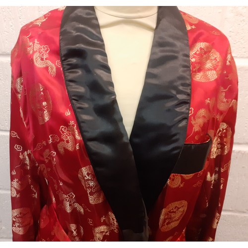 31 - A Chinese red and black smoking robe with machine printed gold embroidered images of dragons having ... 