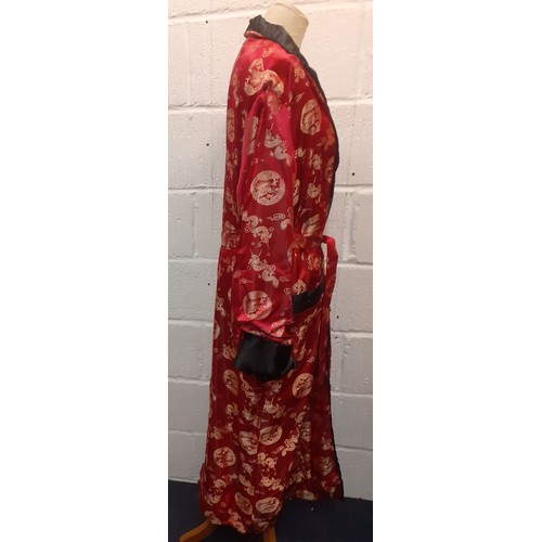 31 - A Chinese red and black smoking robe with machine printed gold embroidered images of dragons having ... 