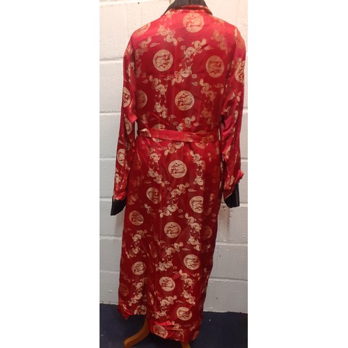 31 - A Chinese red and black smoking robe with machine printed gold embroidered images of dragons having ... 