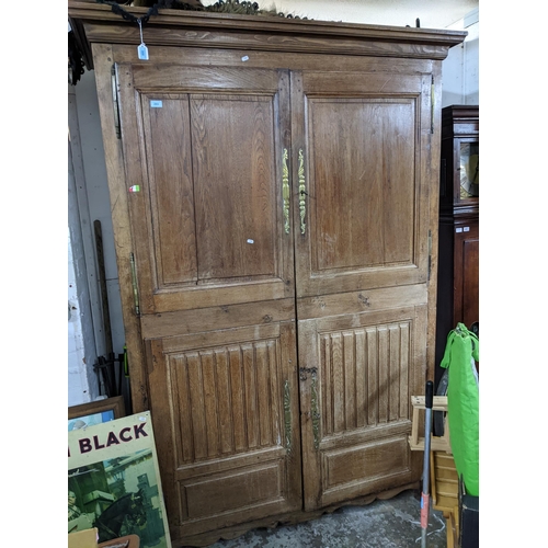 100 - An 18th century oak armoire, twin panelled and carved doors with brass escutcheons, shaped apron and... 