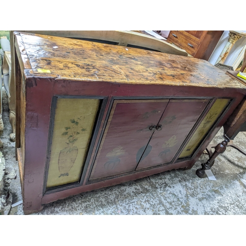 503 - An Asian hardwood side cabinet, twin painted doors decorated with a plant and a bowl of fruit on sta... 