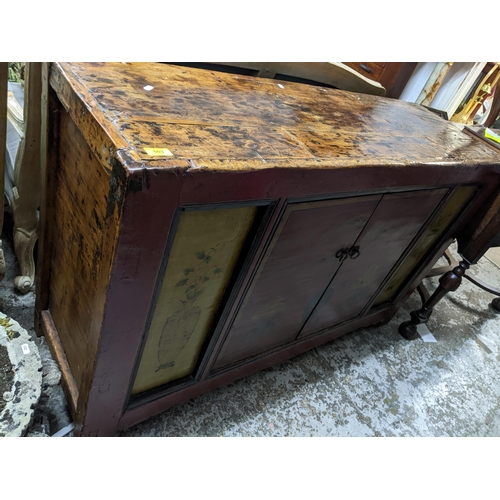 503 - An Asian hardwood side cabinet, twin painted doors decorated with a plant and a bowl of fruit on sta... 