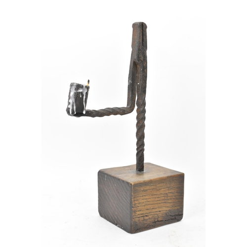 191 - An 18th century wrought iron rush-light holder, with a candle socket arm raised on an oak base, 25cm... 