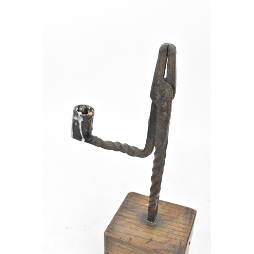 191 - An 18th century wrought iron rush-light holder, with a candle socket arm raised on an oak base, 25cm... 