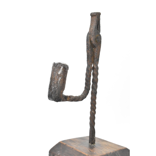 192 - An 18th century wrought iron rush-light holder, with a candle socket arm raised on an oak base, 26cm... 