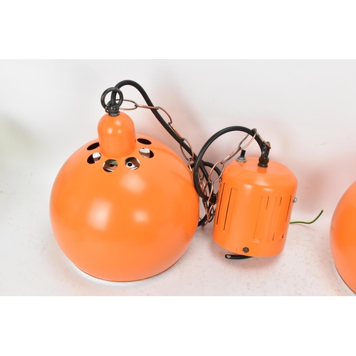 86 - A retro set of three 1970s eyeball hanging lights, each with orange enamel shades and cast iron susp... 