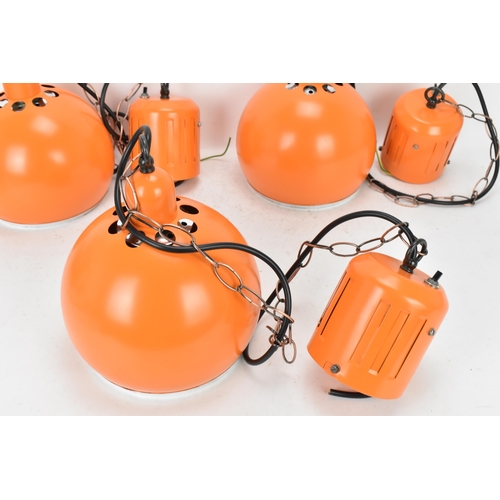 86 - A retro set of three 1970s eyeball hanging lights, each with orange enamel shades and cast iron susp... 