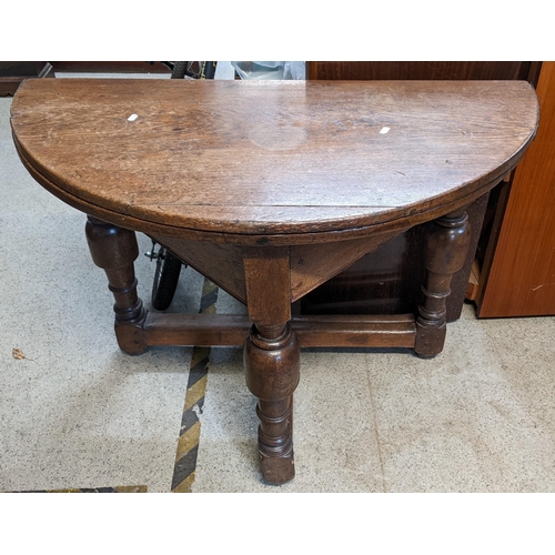 551 - An early 20th century copy of a 17th century oak demi lune fold over table having turned legs, unite... 