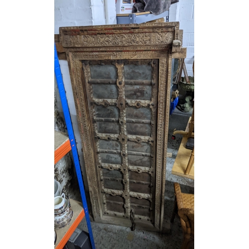 604 - An antique Indian carved and studded hardwood door, fixed into a frame, 174cm high x 80cm wide  Loca... 