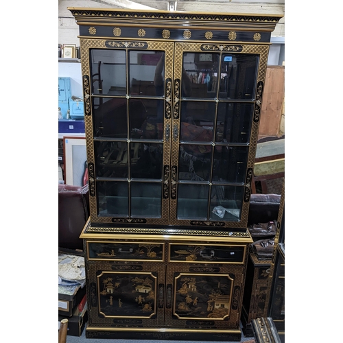 294 - A late 20th century Chinese style black and gilt cabinet with twin glazed panelled doors, over a pai... 