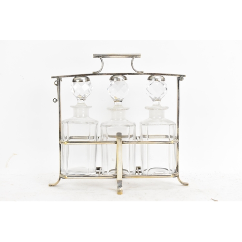 171 - An Art Deco French silver plated liquor tantalus, having three decanters, the frame having a hinged ... 