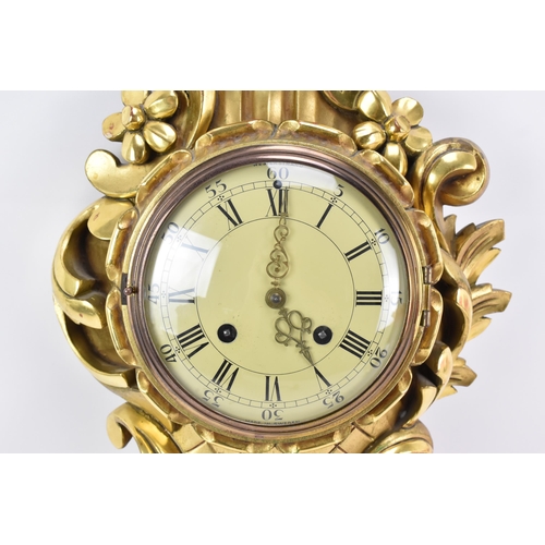 63 - A mid 20th century Louis XVI style giltwood striking cartel wall clock, the ornate case of floral sc... 