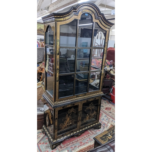 516 - A late 20th century Chinese style black and gilt cabinet with an arched top, over twin glazed doors ... 