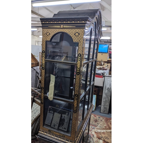 516 - A late 20th century Chinese style black and gilt cabinet with an arched top, over twin glazed doors ... 