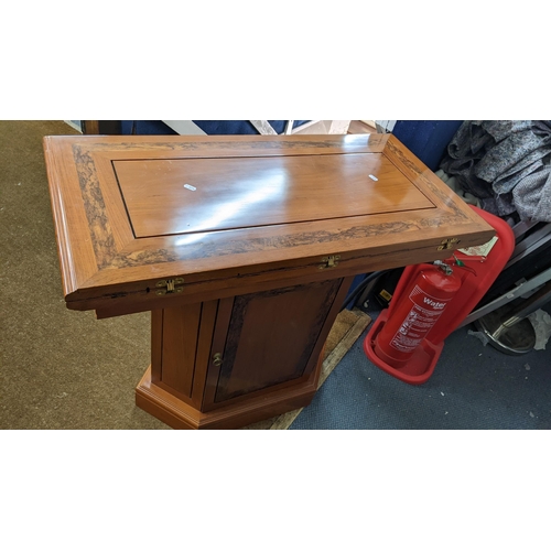 381 - An Indonesian hardwood foldover games table having a swivel top on a pedestal base with a single cup... 