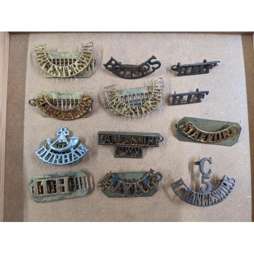 445 - Military cap badges and buttons and regiment name badges, along with a table top display case (glass... 