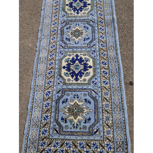 530 - A Moroccan hand woven runner, six central floral medallion, triple guard, on a blue ground with tass... 