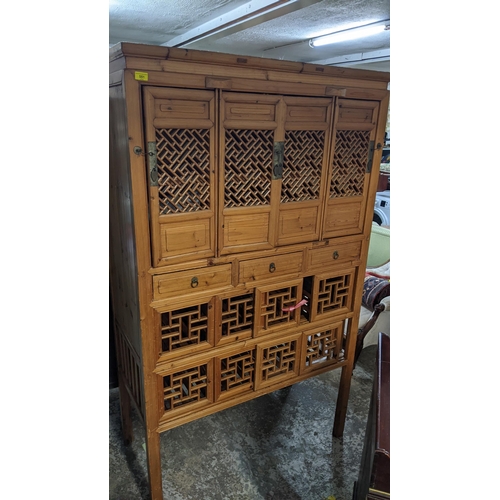 444 - A 20th century Chinese light wood side cabinet having two rows of four sliding doors with pierced de... 