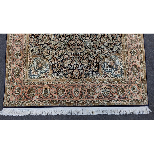 126 - An Indian Kashmir hand woven silk pile rug with a central flower head medallion surrounded by scroll... 