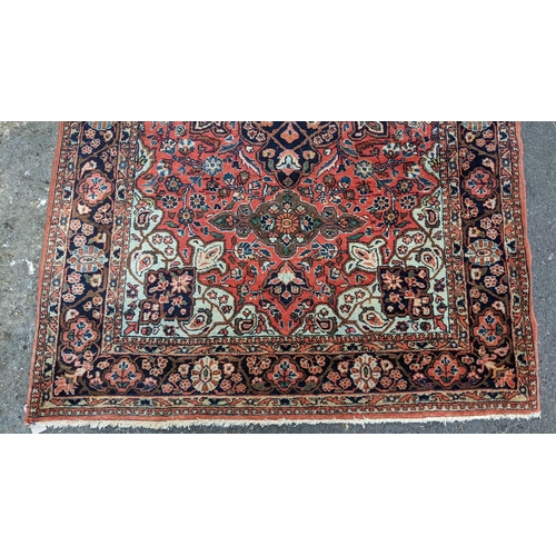 129 - A Persian Sarouk hand woven rug, having a red ground with cenral motif surrounded by vining branches... 