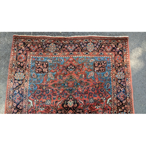 129 - A Persian Sarouk hand woven rug, having a red ground with cenral motif surrounded by vining branches... 