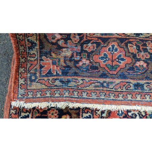 129 - A Persian Sarouk hand woven rug, having a red ground with cenral motif surrounded by vining branches... 