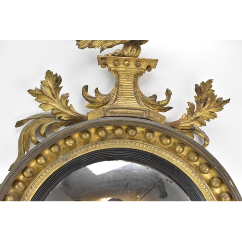 141 - A Regency wall mirror, having a convex plate in a gilt moulded and carved giltwood frame with a ball... 