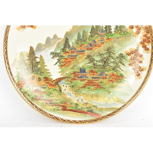 54 - A Japanese Meiji period satsuma dish, by Koshida, the interior decorated with a river scene, buildin... 