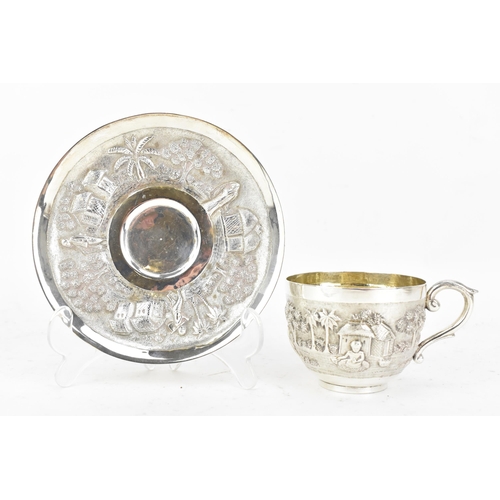 68 - An early 20th century Indian white metal cup and saucer, each embossed with a band depicting a conti... 