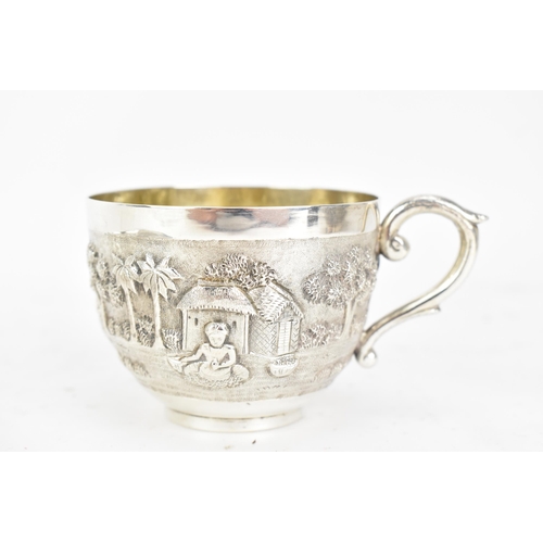 68 - An early 20th century Indian white metal cup and saucer, each embossed with a band depicting a conti... 