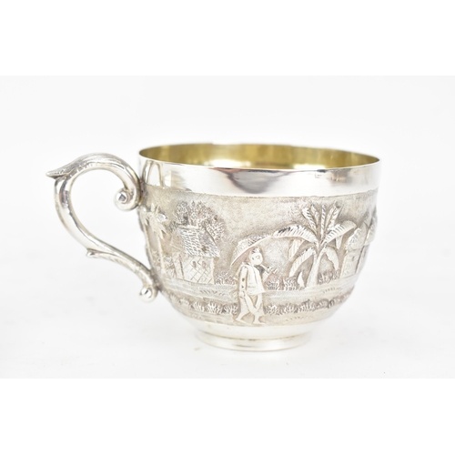 68 - An early 20th century Indian white metal cup and saucer, each embossed with a band depicting a conti... 