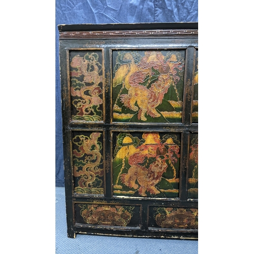 76 - A 19th century Tibetan cabinet, lacquered and polychrome painted with panels depicting foo dogs and ... 