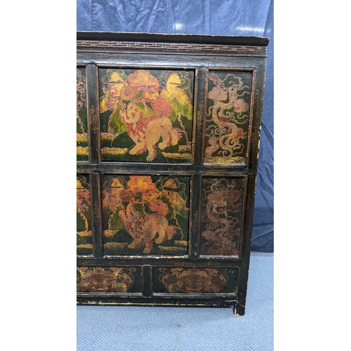 76 - A 19th century Tibetan cabinet, lacquered and polychrome painted with panels depicting foo dogs and ... 