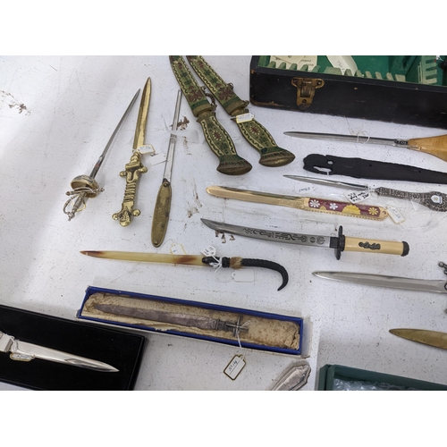 265 - A collection of vintage paper knives, small ornamental daggers and a silver plate meat skewer, conta... 