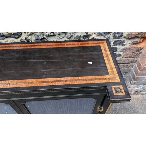 132 - A Regency ebonised chiffonier having two glazed doors, fitted with a loose shelf, flanked by two bra... 