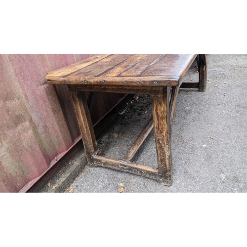 148 - An 18th century vernacular oak dining table, having a plank constructed top, four chamfered legs uni... 