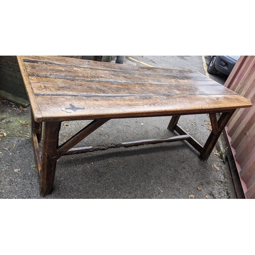 148 - An 18th century vernacular oak dining table, having a plank constructed top, four chamfered legs uni... 