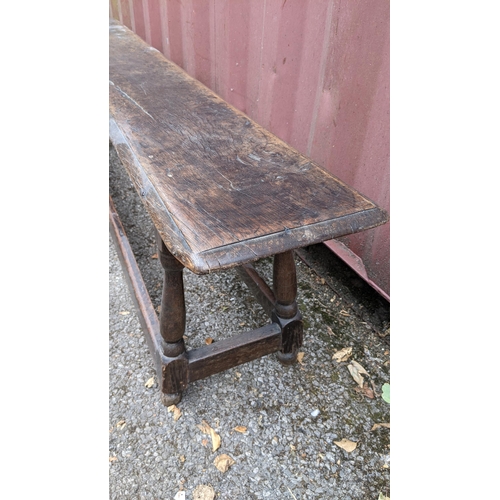 167 - An 18th century oak bench, having a single plank top, above four knop turned columns, united by stre... 