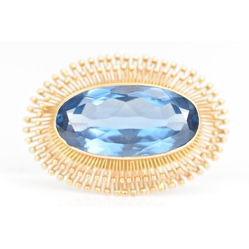 103 - A 14ct gold oval formed brooch, set with a large faceted cut blue stone 30.5mm x 15mm, surrounded by... 