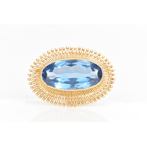 103 - A 14ct gold oval formed brooch, set with a large faceted cut blue stone 30.5mm x 15mm, surrounded by... 