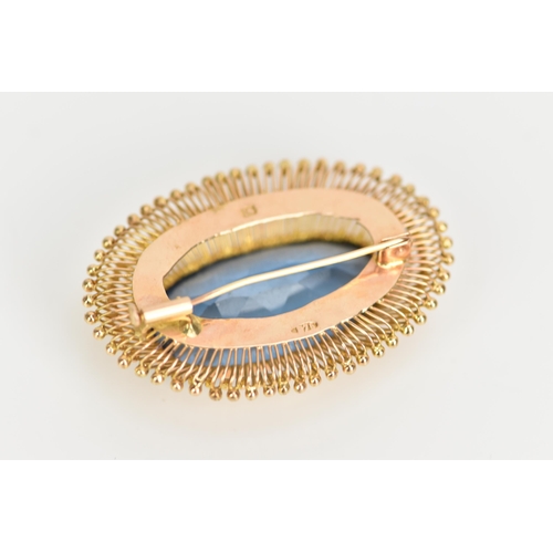 103 - A 14ct gold oval formed brooch, set with a large faceted cut blue stone 30.5mm x 15mm, surrounded by... 