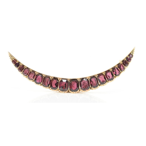 145 - An Edwardian yellow metal crescent brooch, inset with nineteen faceted cut graduating garnets, large... 