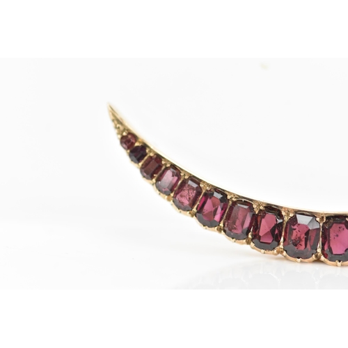 145 - An Edwardian yellow metal crescent brooch, inset with nineteen faceted cut graduating garnets, large... 