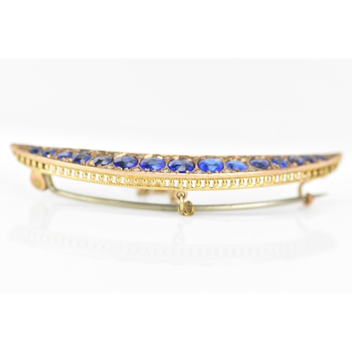 146 - An Edwardian 9ct gold crescent brooch, inset with fifteen blue coloured graduating stones and twelve... 