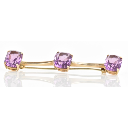 182 - An Edwardian yellow metal bar brooch, with three faceted cut amethysts in four claw settings, each s... 