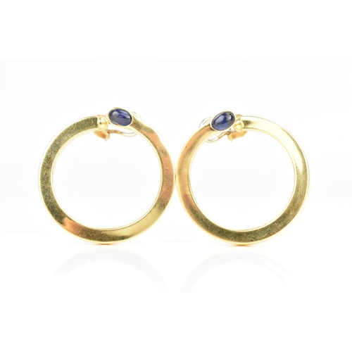 205 - A pair of 18ct yellow gold hoop earrings, each inset with a blue sapphire cabochon, stamped 750, 35.... 