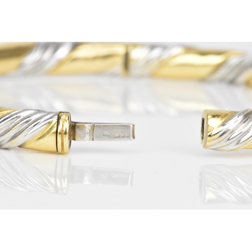 54 - An 18ct gold bi-coloured bangle, having a gadrooned design alternating in yellow and white gold, sta... 