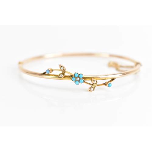 70 - A 10ct gold bangle inset with turquoise and seed pearls, having a floral design with seven turquoise... 