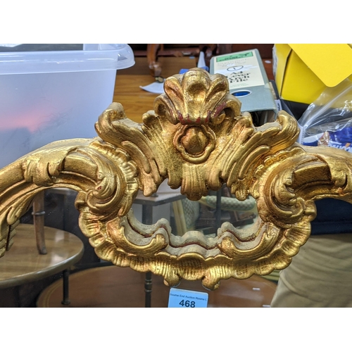 468 - A gilt framed overmantel mirror decorated with gold coloured gilding with a central emblem at the to... 