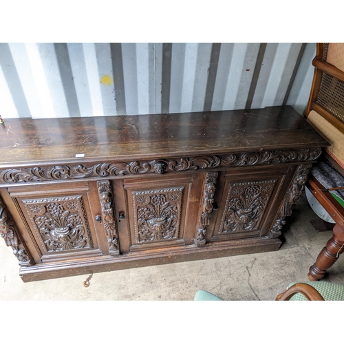 531 - An early 20th century oak sideboard with carved ornament, and three doors on a plinth, 99cm h x 181c... 